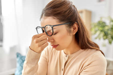 tired asian woman with glasses rubbing nose bridge