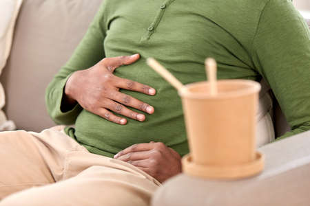 close up of overeaten man and cup of takeaway food
