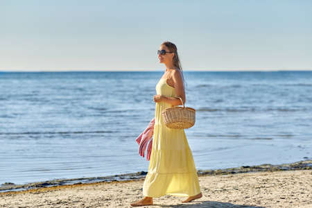 happy woman with picnic basket walking along beachの写真素材