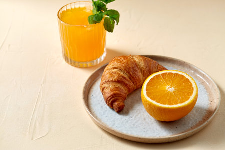 glass of orange juice and croissant on plateの写真素材