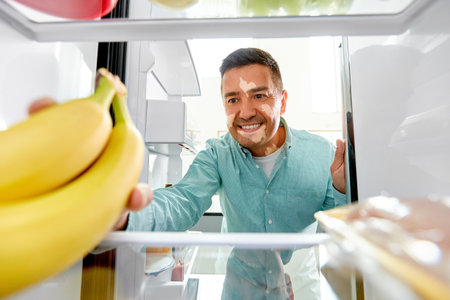man with vitiligo taking banana from fridgeの写真素材