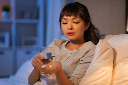 stressed asian woman taking medicine at nightの写真素材