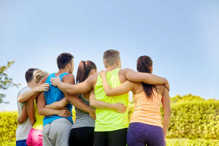 group of happy sporty friends hugging outdoors