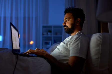 indian man with laptop in bed at home at nightの写真素材