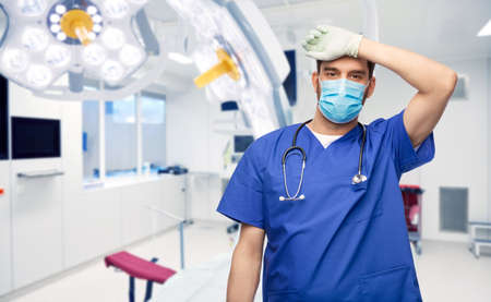 tired male doctor in blue uniform, mask and gloves