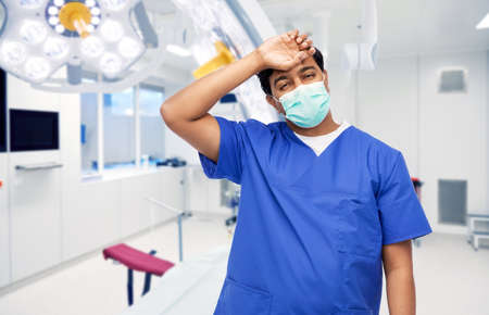 tired indian male doctor in blue uniform and maskの写真素材