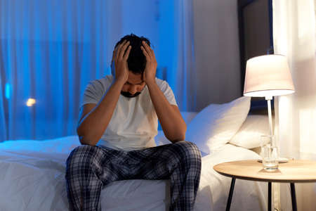 stressed indian man sitting on bed at nightの写真素材