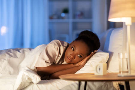 sleepless african woman lying in bed at nightの写真素材