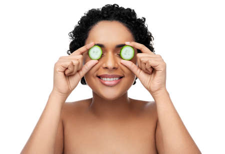 happy african woman making eye mask of cucumbers