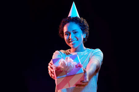 african woman in party cap with gift box on black