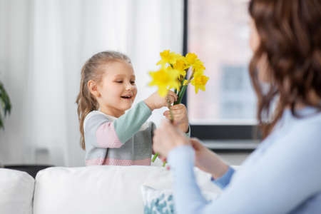 happy daughter giving daffodil flowers to motherの写真素材