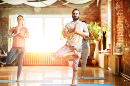 group of people doing yoga tree pose at studioの写真素材