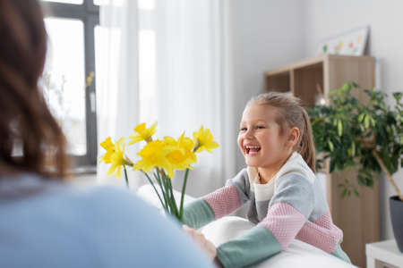 happy daughter giving daffodil flowers to motherの写真素材