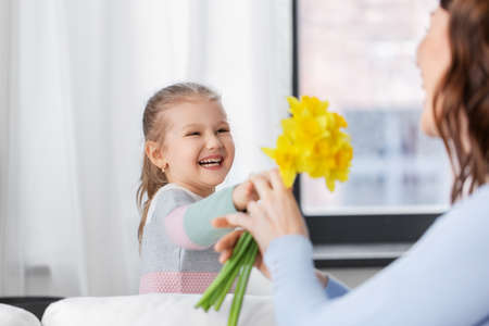 happy daughter giving daffodil flowers to motherの写真素材