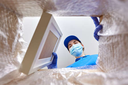 woman in mask packing photo frame to parcel box