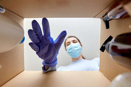 woman in mask unpacking parcel box with cosmetics