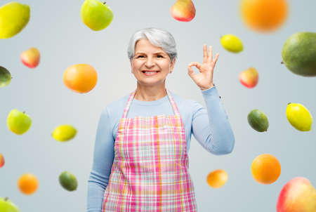 smiling senior woman in apron showing ok gesture