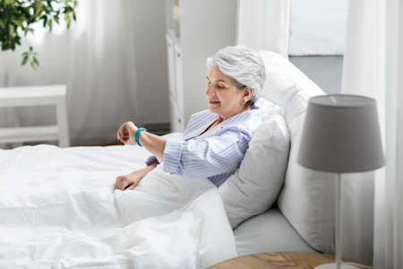happy old woman with health tracker sitting in bedの写真素材