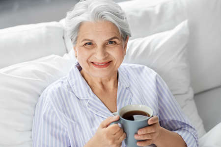 old woman with cup of coffee in bed at home