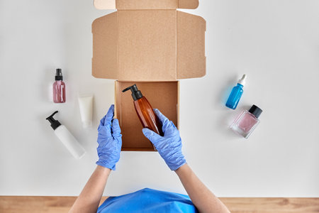 hands in gloves packing parcel box with cosmeticsの写真素材
