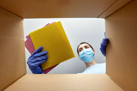 woman in mask taking cleaning supplies from boxの写真素材