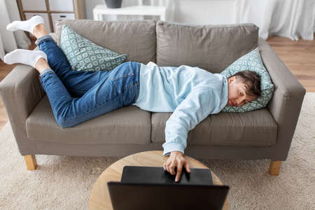 bored man with laptop lying on sofa at home