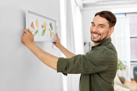 smiling man decorating home with picture in frameの写真素材