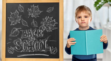 little displeased student boy with bookの写真素材