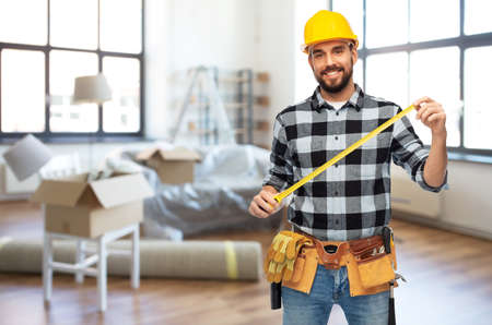 happy male builder in helmet with ruler at homeの写真素材