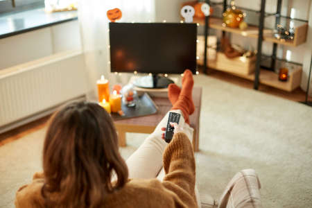 young woman watching tv at home on halloweenの写真素材