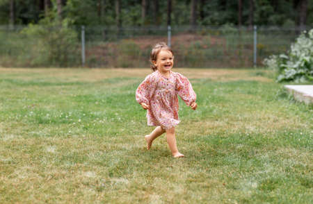 happy little baby girl running barefoot on grassの写真素材