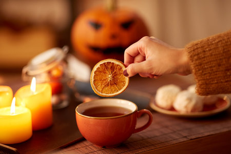 hand adding dry orange to cup of tea on halloweenの写真素材