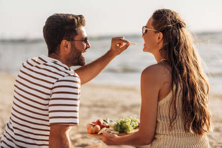happy couple with food having picnic on beachの写真素材