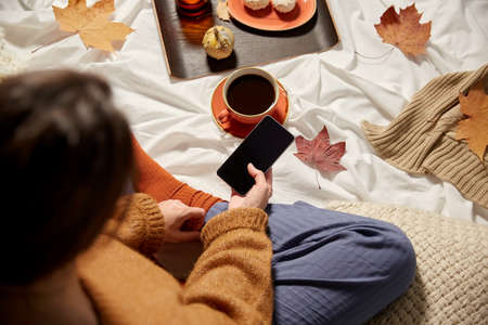 woman with smartphone at home in autumnの写真素材