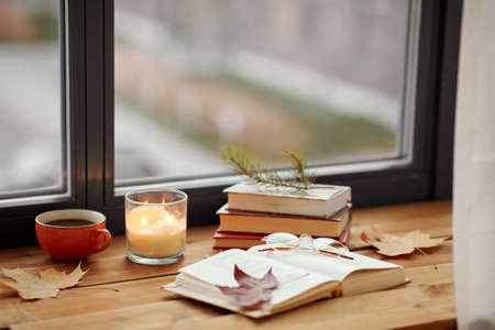 book, coffee and candle on window sill in autumn