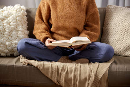 woman in warm sweater reading book at home