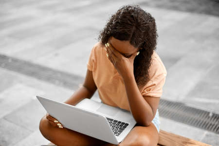 stressed african student girl with laptop in cityの写真素材