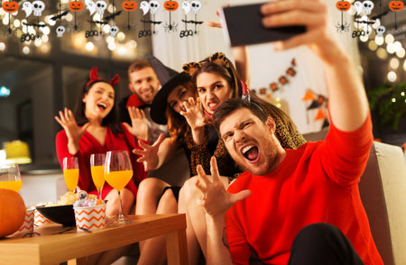happy friends in halloween costumes taking selfieの写真素材