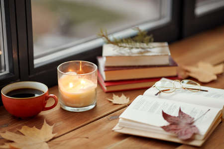 book, coffee and candle on window sill in autumnの写真素材