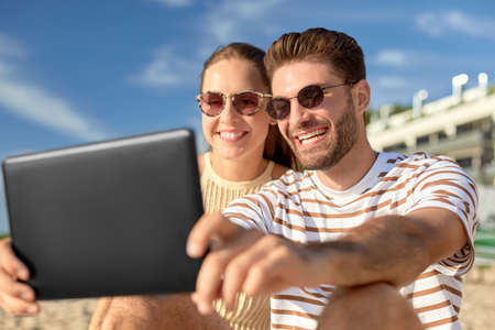 happy couple with tablet pc at on summer beach