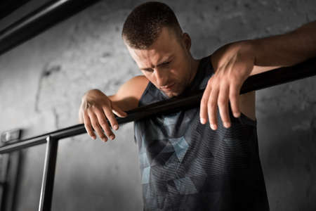 tired young man at parallel bars in gym