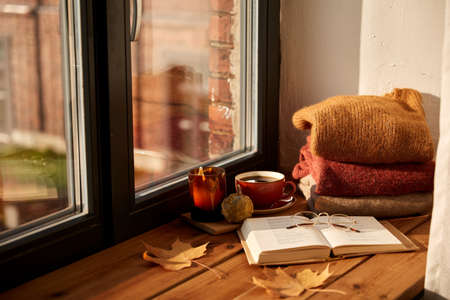 book, coffee and candle on window sill in autumn