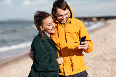 couple with smartphone on autumn beachの写真素材