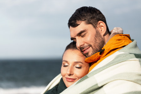 happy couple in warm blanket on autumn beach
