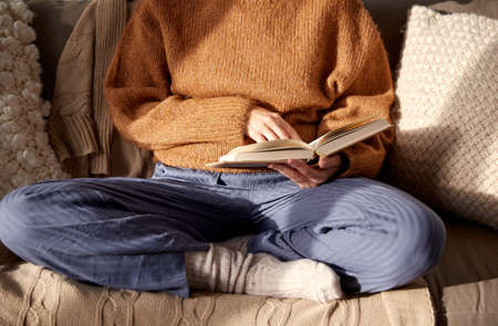 woman in warm sweater reading book at homeの写真素材