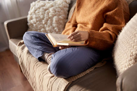 woman in warm sweater reading book at homeの写真素材