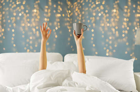 woman with cup of coffee lying in bed showing okの写真素材