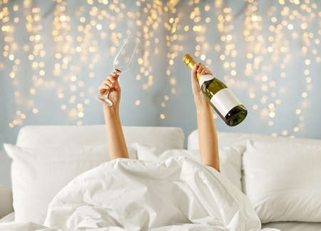 hands of woman lying in bed with champagneの写真素材