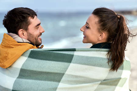 happy couple in warm blanket on autumn beachの写真素材