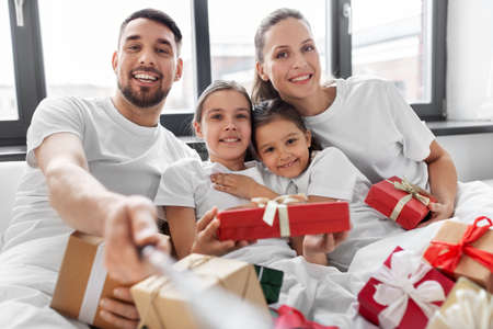 family with christmas gifts taking selfie in bedの写真素材